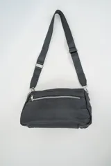 Bandolera negra con cierre principal y bolsillo frontal con cierre, ambos con cremalleras plateadas. Tiene una correa ajustable de tela negra.