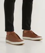 Championes marrones de cuero, con caña baja, ajuste con cordones y suela blanca.