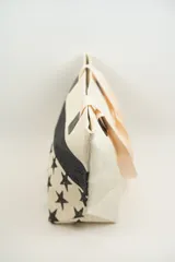 Bolso tipo tote con estampado de estrellas negras sobre fondo beige y una franja horizontal negra con glitter.