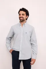 Camisa celeste con rayas verticales finas en blanco y azul, de manga larga y corte clásico. Tiene bolsillo en el pecho y cuello abotonado.