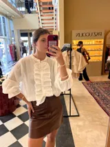 Camisa blanca de manga larga con volados frontales y cuello mao, confeccionada en tela ligera para un estilo elegante y femenino.