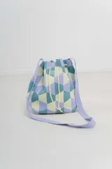 Bolso tipo bucket tejido con diseño geométrico en tonos lila, celeste y amarillo. Tiene cordón ajustable y correa ancha al tono para llevar al hombro o cruzado.