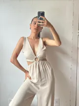 Mono largo color crudo, con escote en V, corte en la cintura con detalle de aro metálico y aberturas laterales.