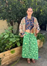 Camisa crop azul con estampado floral multicolor, cuello camisero, mangas largas con puños abotonados y lazos para atar en la cintura.
