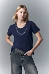 Remera blanca de algodón con cuello redondo y aplique de cadenas metálicas y strass en el escote.