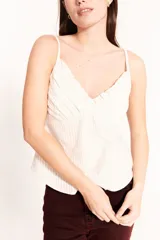 Musculosa color crema a rayas finas, con breteles finos, escote en V con volados y detalle de pinzas en el busto.