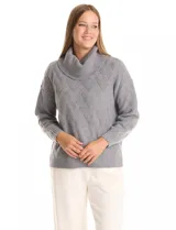 Buzo de punto grueso color beige, con cuello volcado y textura en relieve. Tiene mangas largas de corte hombro caído y puños anchos.