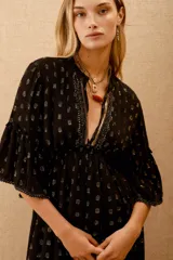 Vestido largo negro con estampado de lunares dorados, mangas al codo y corte amplio con ajuste elástico en la cintura. Presenta bordados de lentejuelas y mostacillas en el escote y mangas.