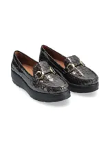 Mocasín de cuero charol negro con plataforma blanca y detalle de hebilla metálica plateada en el empeine.