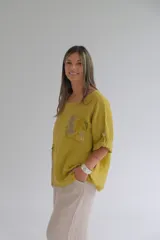 Blusa color mostaza de corte holgado, con cuello redondo, mangas 3/4 con botón para sujetar y detalle de bolsillo y aplique floral en la parte inferior.