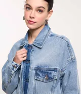 Campera de jean celeste, corte cropped y holgado, con cuello camisero, cierre abotonado, mangas largas, bolsillos con solapa en el pecho y recortes verticales.