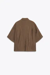 Camisa rosa de cuello solapa y manga corta con vuelta. Bajo asimétrico con aberturas laterales. Cierre frontal con botones ocultos por solapa.