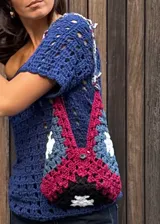 Cartera tejida a crochet, con diseño geométrico multicolor y asa corta.