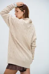 Sweater de punto trenzado color beige, con cuello en V y cuello polo, de manga larga y corte holgado.