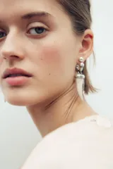 Aros metálicos plateados con colgante de cuerno de resina color crema. Cierre con tuerca.