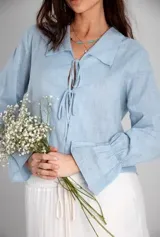 Camisa celeste de lino con cuello clásico, mangas largas con puños elásticos y lazos en el escote.