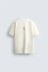Camiseta color crudo de corte holgado, cuello redondo y manga corta. Tiene estampado de salpicaduras de pintura negra en el frente y texto estampado en la espalda.