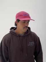 Gorro tipo gorra color fucsia con visera, y estampado frontal en azul con la palabra "attitude" y otros textos.