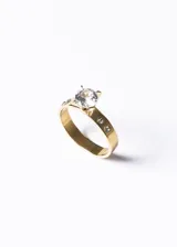 Anillo dorado de acero quirúrgico con piedra central brillante y pequeñas piedras laterales.