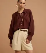 Short de mujer color beige claro, de cintura alta y corte holgado, con pliegues frontales y cierre tradicional. Incluye un cinturón fino de material sintético marrón.