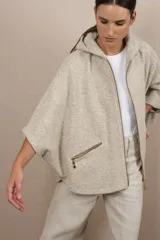 Capa amplia color beige con capucha y cierre frontal con cremallera dorada. Tiene bolsillos laterales con cierre. Confeccionada en lana fina sin teñir, diseñada por Don Baez.