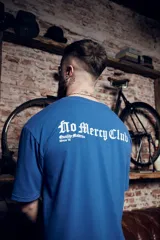 Remera azul con estampado en tinta blanca y dorada con la frase "No Mercy Club Quality Matters Since 19". Corte oversized más amplio en la parte trasera.