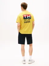 Remera amarilla de algodón con corte amplio, cuello redondo y hombros caídos. Presenta un logo pequeño de Tommy Hilfiger en el pecho, un logo en la manga y un logo grande en la espalda. Pertenece a la colección Hilfiger Sailing.