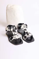 Sandalias planas con tiras de cuero con estampado de vaca en blanco y negro, y hebilla lateral.