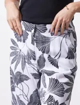 Pantalón de lino blanco con estampado de hojas en negro, de corte recto y pretina ancha con pasadores. Tiene bolsillos delanteros y bolsillos ojal simulados en la parte trasera.