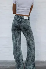 Jean de mujer de corte recto y tiro alto, con efecto acid wash en tonos gris y verde claro. Presenta costuras frontales y traseras que simulan pliegues, y etiqueta de marca blanca en la parte trasera de la cintura.