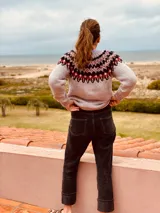 Sweater gris con diseño geométrico en negro y rojo alrededor del cuello, de lana tejido a mano con estilo nórdico.
