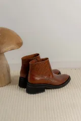 Bota corta color marrón con textura símil cuero de cocodrilo, caña baja, punta redondeada y taco cuadrado.