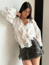 Blusa negra traslúcida con volados, mangas largas abullonadas y cierre frontal con botones.