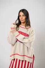 Sweater tejido color crudo con cuello redondo y mangas largas. Presenta dos peces rojos con detalles en azul bordados en el frente. Tiene ribete ondulado rojo en cuello, puños y ruedo.