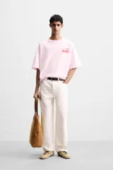 Camiseta rosa de corte holgado, cuello redondo y manga corta. Estampado frontal con texto en rojo "Amalfi Coast" y estrellas.