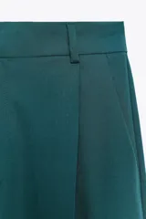 Pantalón marrón de tiro alto con trabillas, doble pliegue, bolsillos laterales y de vivo en la espalda, pernera ancha y cierre frontal con cremallera y gancho metálico.