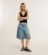 Bermuda de jean azul claro, modelo jorts, con trabillas en la cintura y bolsillos. Presenta un cordón blanco decorativo atado en el bolsillo delantero.