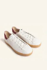 Zapatillas bajas blancas de cuero vacuno con detalle de refuerzo de gamuza color borgoña en el talón y suela de goma color caramelo.