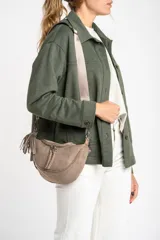 Riñonera color arena de gamuza vegana con correa ancha de poliéster color rosa claro. Tiene cierre superior, bolsillo interno y detalle de flecos en el lateral.