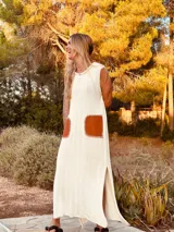 Vestido largo tejido en hilo de algodón color crudo, sin mangas, con tajos laterales y bolsillos de cuero marrón.