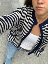 Chaqueta tejida a rayas horizontales azul marino y crudo, con cuello redondo, mangas 3/4 y bolsillos frontales.