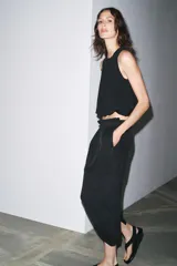 Falda midi negra de tiro alto con cintura elástica y frunces. Presenta detalle de tejido combinado y abertura en la parte trasera del ruedo.
