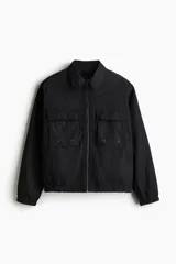 Campera negra con cuello camisero, cierre frontal y bolsillos superiores con solapa. Elástico revestido en puños y bajo.
