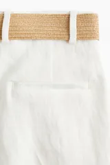 Short blanco de sarga con cinturón ancho extraíble de rafia con hebilla cuadrada con detalle de perlas. Modelo de corte holgado con tiro alto, bolsillos laterales discretos, bolsillos atrás insertados y cierre con botón y corchete ocultos. Piernas con pinzas y pliegues adelante y atrás.