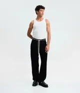 Pantalón masculino negro de corte baggy, confeccionado en sarga de algodón. Presenta detalles de costura, cierre tradicional de botón y cremallera, y un cordón blanco para ajustar la cintura.