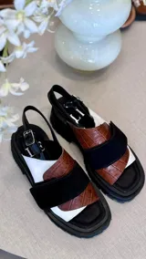 Sandalias marrones con tiras anchas de cuero texturizado y gamuza, suela track negra y hebilla ajustable en el tobillo.