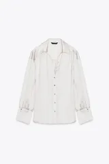 Camisa color blanco hueso de satén, con cuello solapa, escote en pico y mangas largas con puños abotonados.