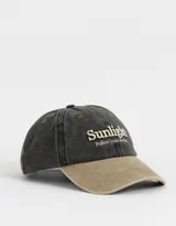 Gorra de gabardina color gris oscuro con visera color beige. Tiene bordado frontal con la palabra "Sunlight" y la frase "Follow your destiny".