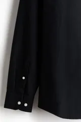 Camisa negra de algodón Oxford con cuello americano, tapeta clásica, bolsillo superior abierto y canesú en la espalda. Mangas largas con puños abotonados y bajo levemente redondeado. Corte estándar para una silueta clásica y cómoda.