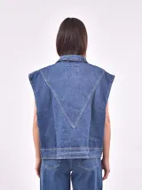 Chaleco de denim azul lavado, sin mangas, con cuello camisero, botones frontales y bolsillos de parche en el pecho.